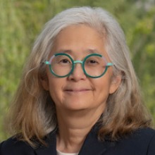 A person with round green glasses and gray shoulder-length hair