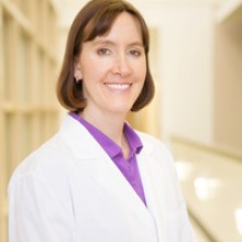 Person with short dark hair wearing a white lab coat and purple blouse.